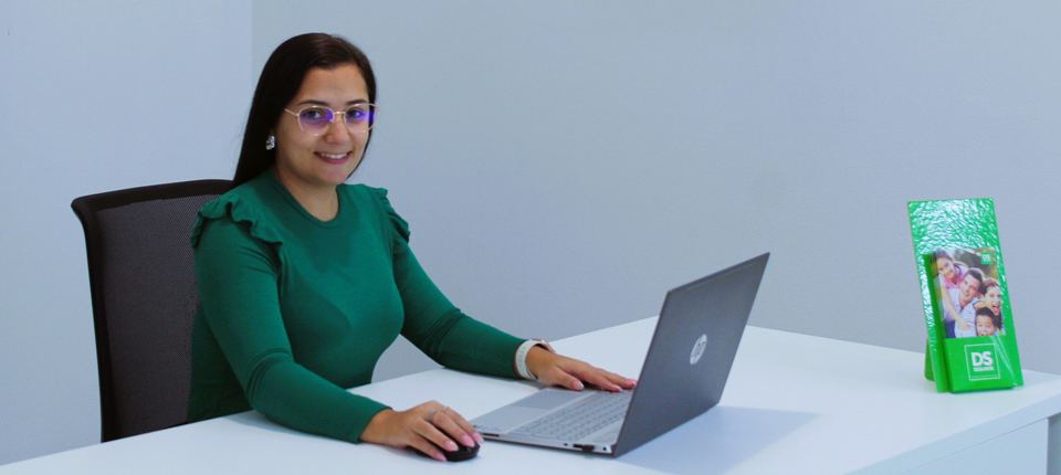 Atendimento na agência DS Seguros em Buarcos: uma colaboradora sorri ao computador, com material DS Seguros na secretária.